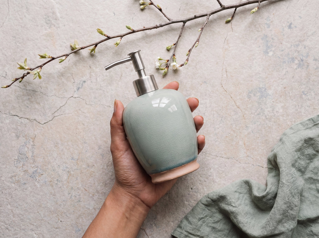 A hand holding the celadon ceramic soap dispenser to show its size
