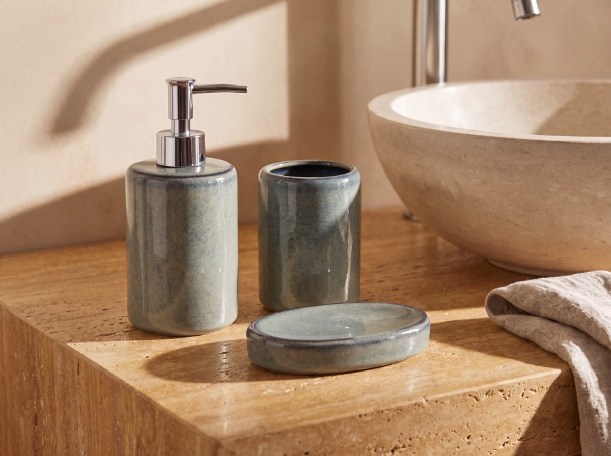 The blue-green ceramic bathroom set arranged on a travertine vanity beside a stone basin and linen towel.
