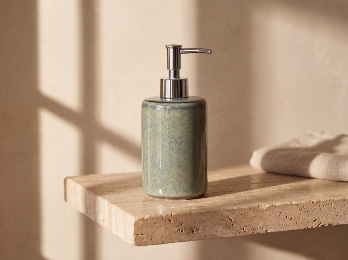The blue-green ceramic soap dispenser alone on a thick sunlit stone shelf with long afternoon shadows.