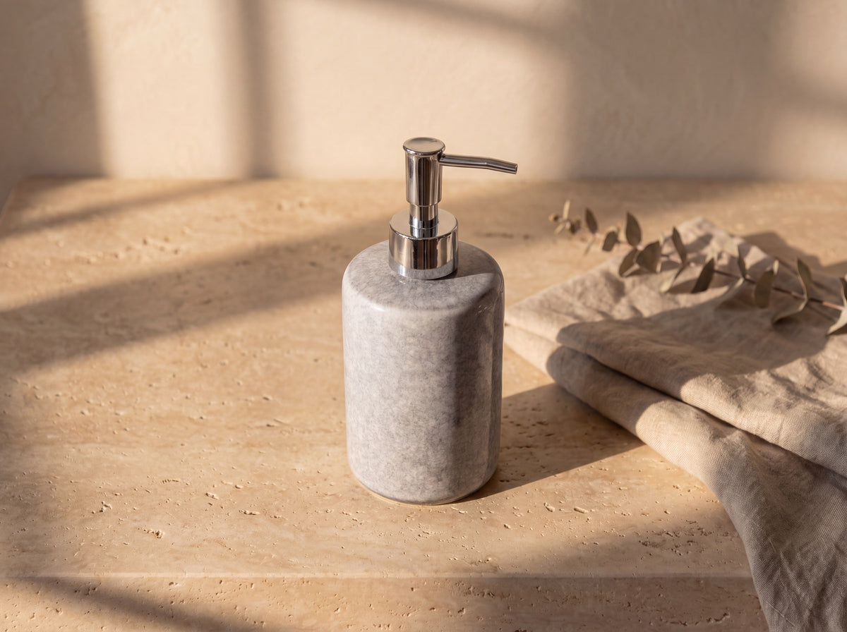 High three-quarter view of the grey ceramic dispenser showing its rounded shoulder and chrome pump.