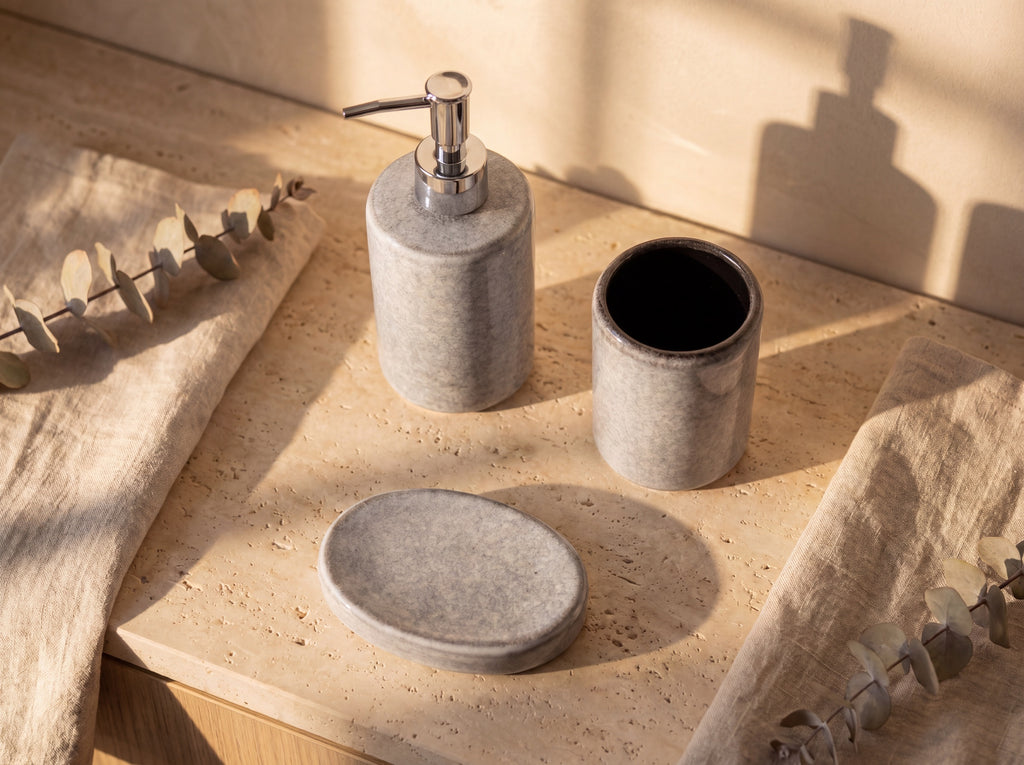 High-angle view of the grey ceramic bath set: dispenser, holder with black glazed interior, and flat oval soap dish.