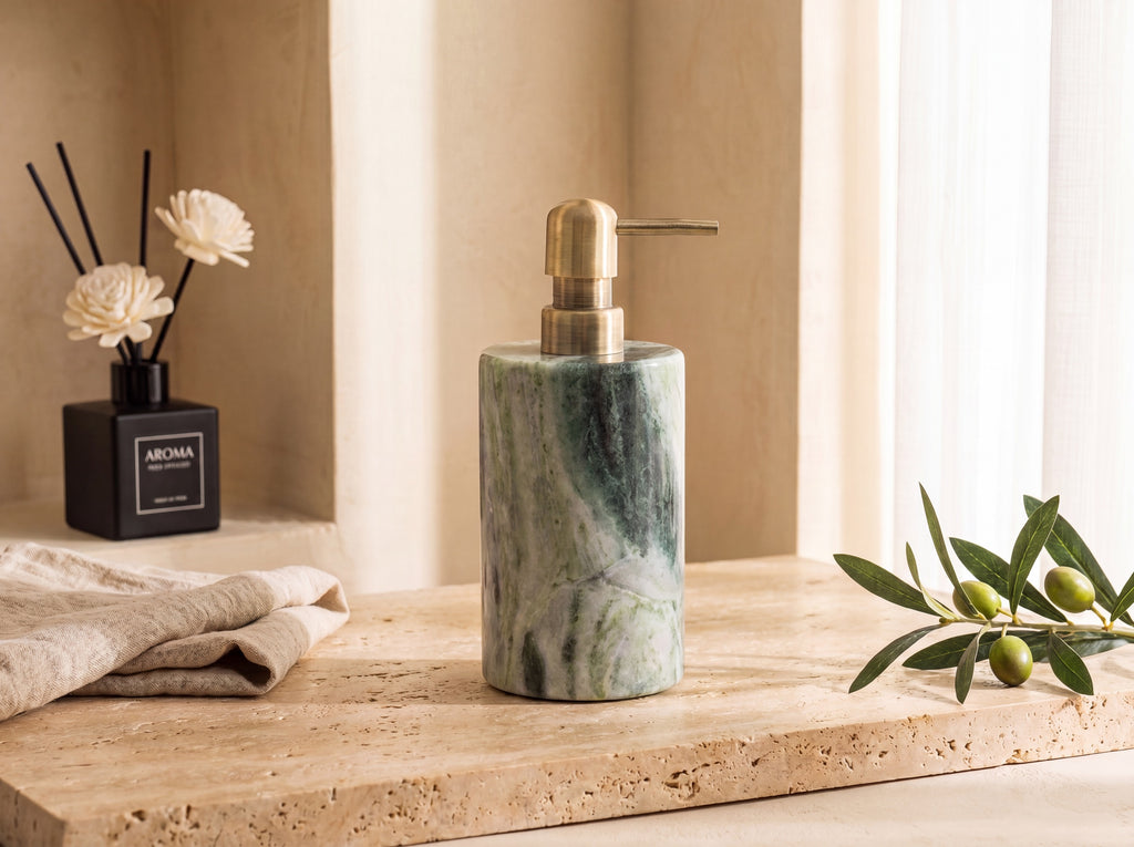 Three-quarter view of a green marble lotion dispenser showing the brushed brass pump and veined stone body against a warm plaster wall.