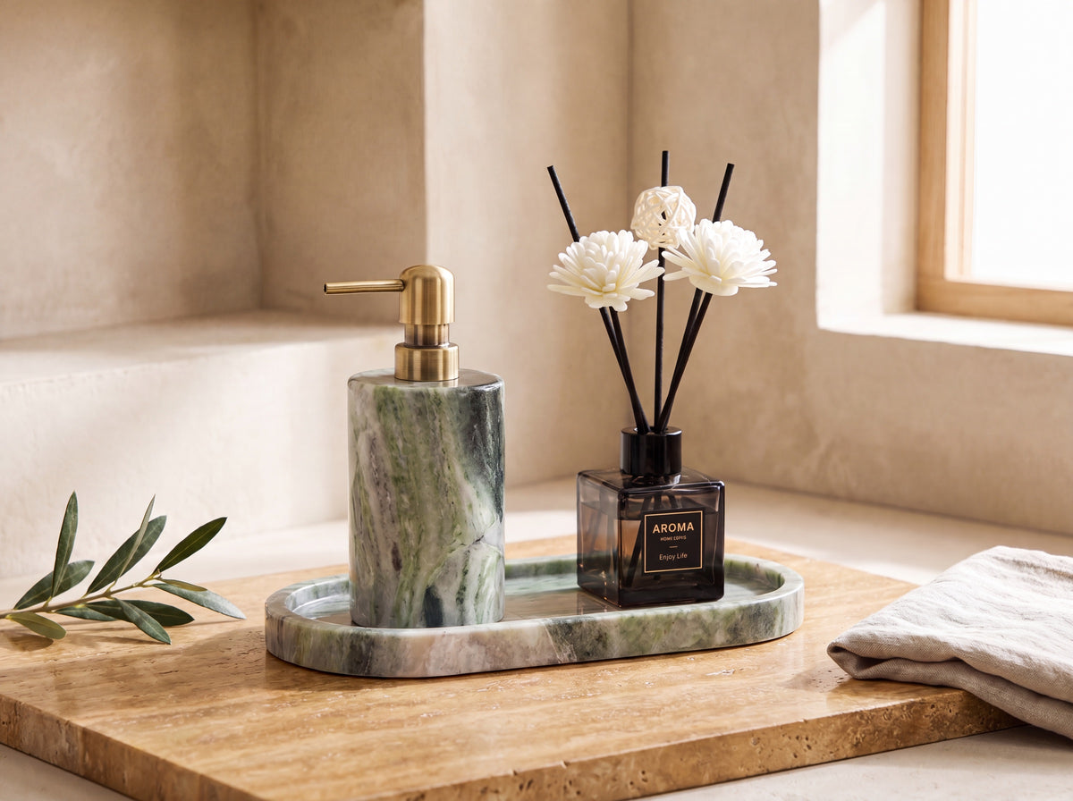 Green marble lotion dispenser and black reed diffuser with white sola flowers on a matching oval green marble tray, warm travertine styling.