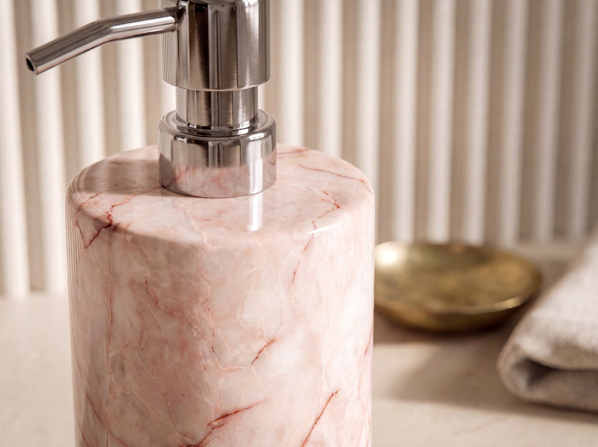 Close-up of blush marble veining and the chrome pump base on a natural stone soap dispenser, showing rust-red veins in the polished stone.