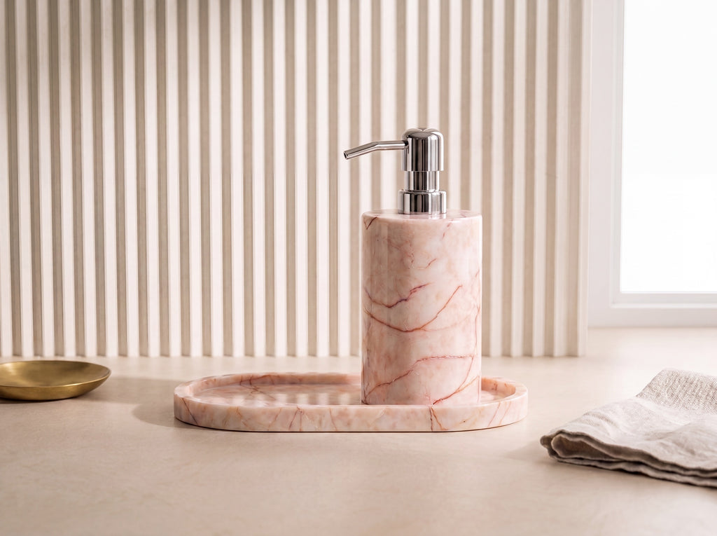 Elevated three-quarter view of a pink marble soap dispenser and oval tray set on a fluted cream backdrop.