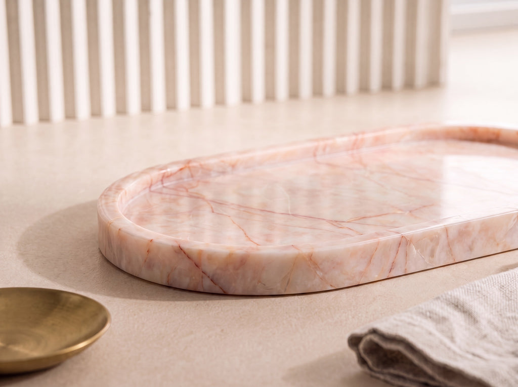 Close-up of an oval blush marble tray showing rose and rust veining and the low rounded wall on a natural stone surface.