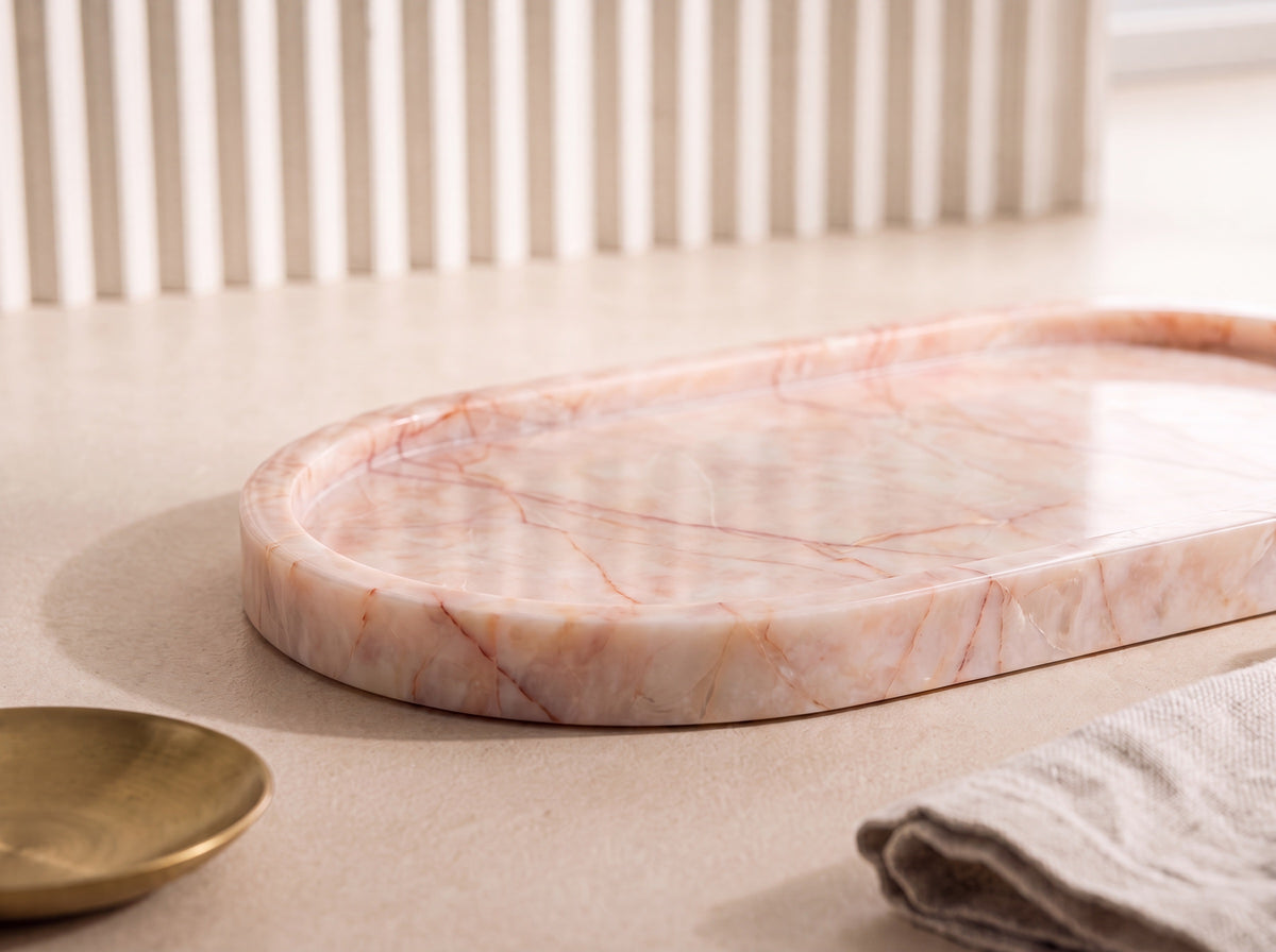 Close-up of an oval blush marble tray showing rose and rust veining and the low rounded wall on a natural stone surface.