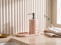 Pink marble dispenser and tray set styled on a bright luxury bathroom vanity with eucalyptus, linen and a brass dish.