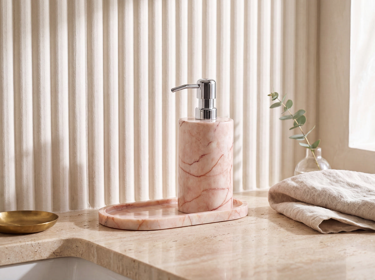 Pink marble dispenser and tray set styled on a bright luxury bathroom vanity with eucalyptus, linen and a brass dish.