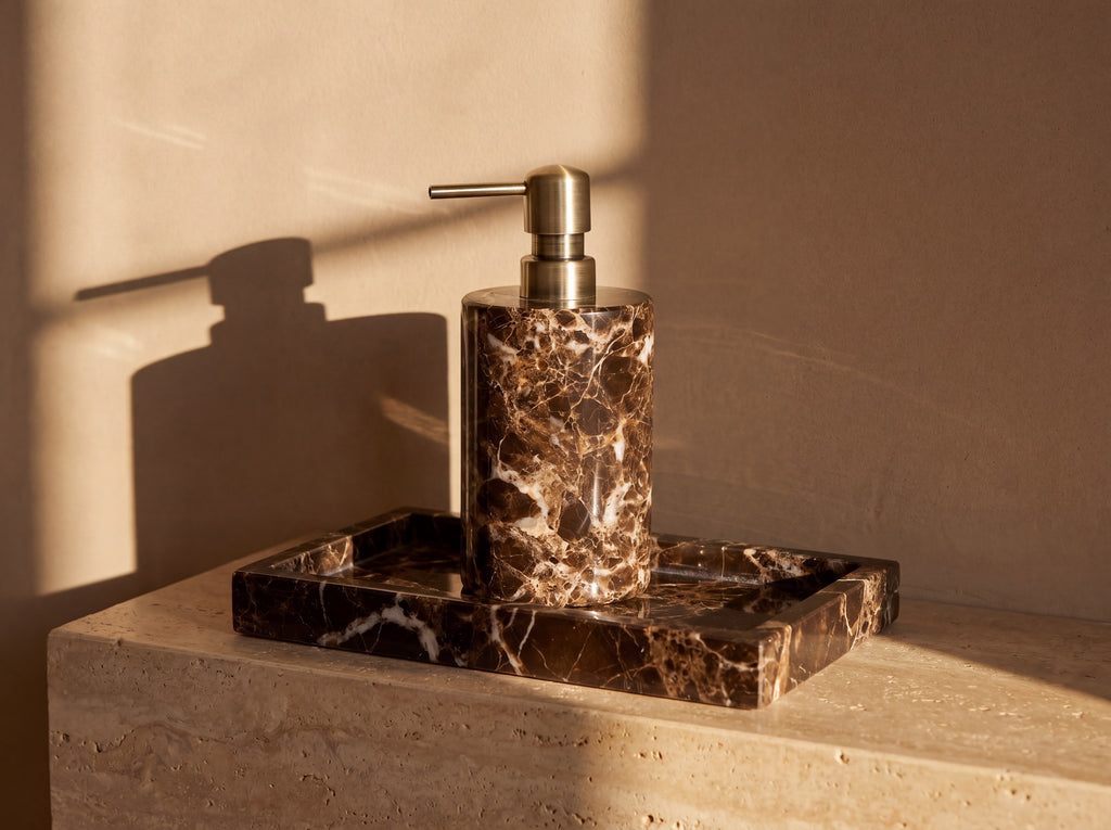 Dark marble soap dispenser standing on a rectangular marble tray with raised walls, both cut from the same brown white-veined stone.