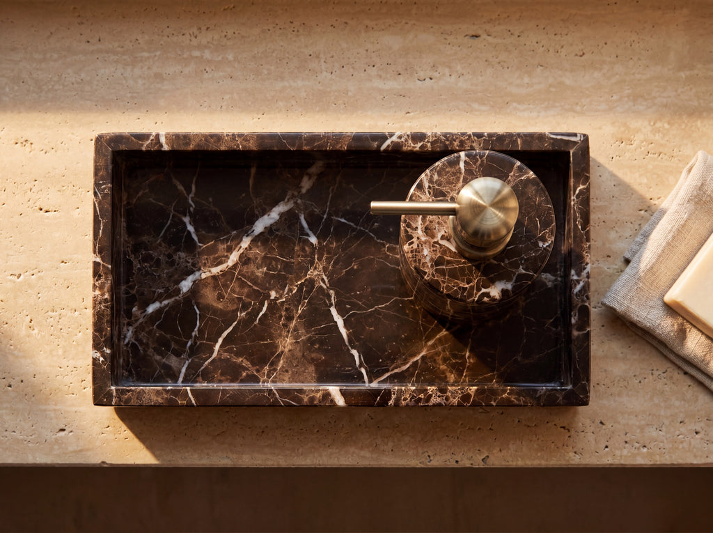 Overhead view of a rectangular dark marble tray holding a round marble soap dispenser, with a linen cloth and cream soap bar alongside.