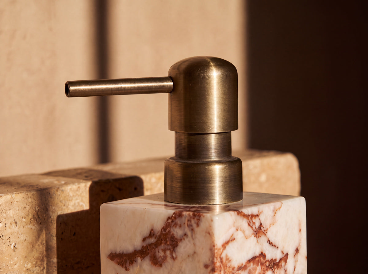 Close-up of the antique brass pump head and the rust-red veining running through the creamy marble column beneath it.