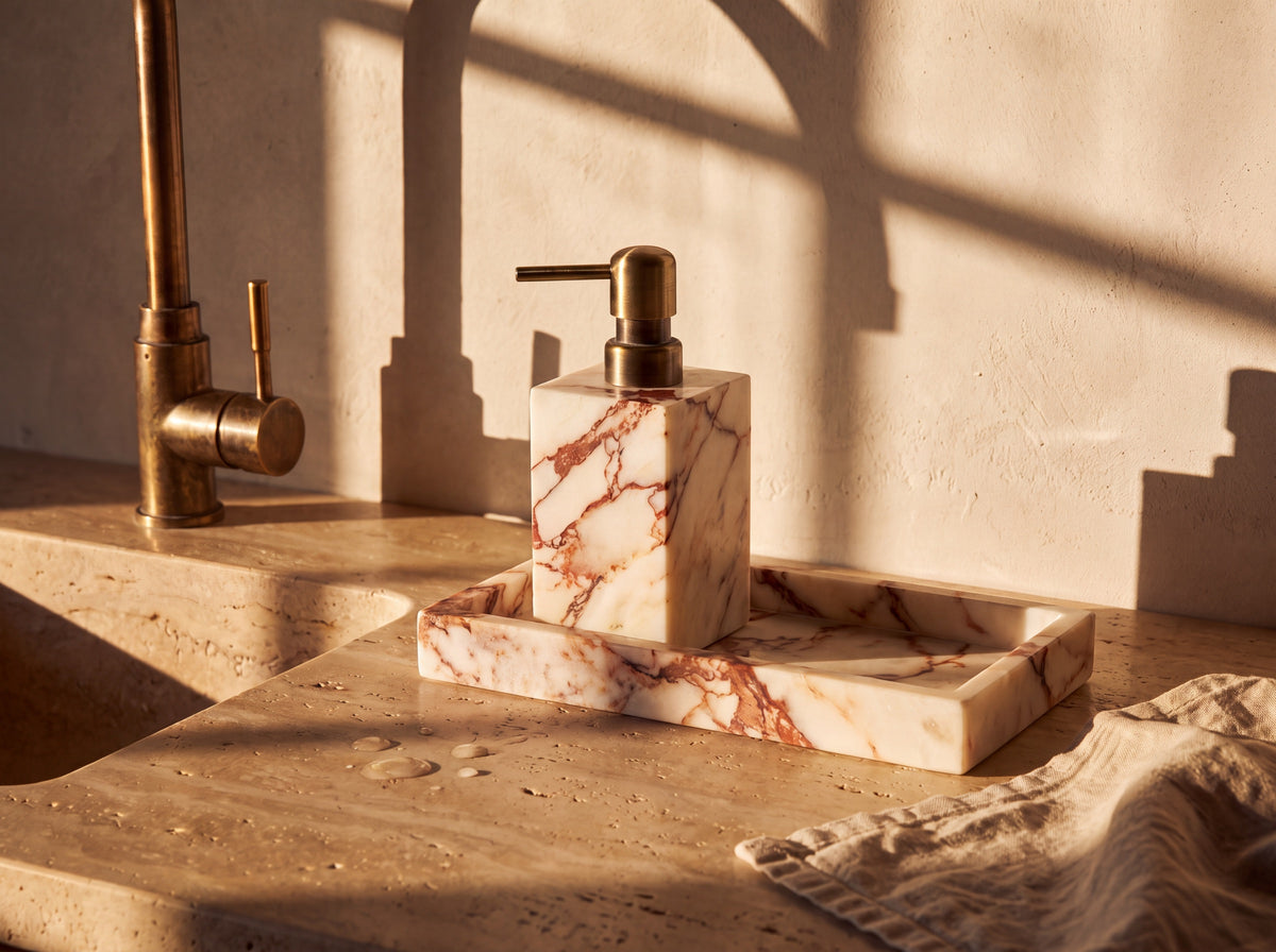 Marble soap dispenser on its marble tray beside a stone kitchen sink with a wooden dish brush and linen tea towel.