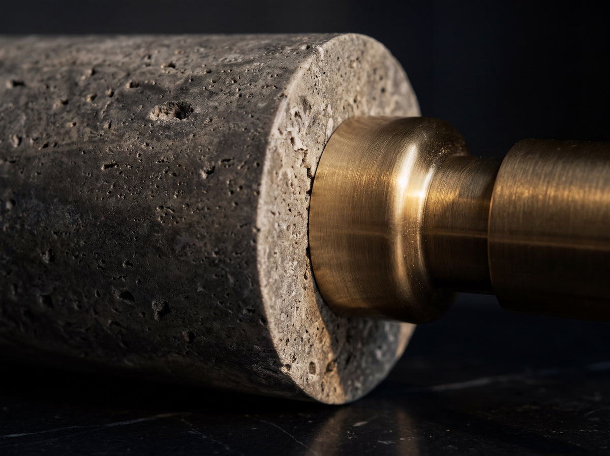 Close-up of natural pitted travertine stone texture meeting the brushed brass pump base of a marble soap dispenser, background falling to shadow.