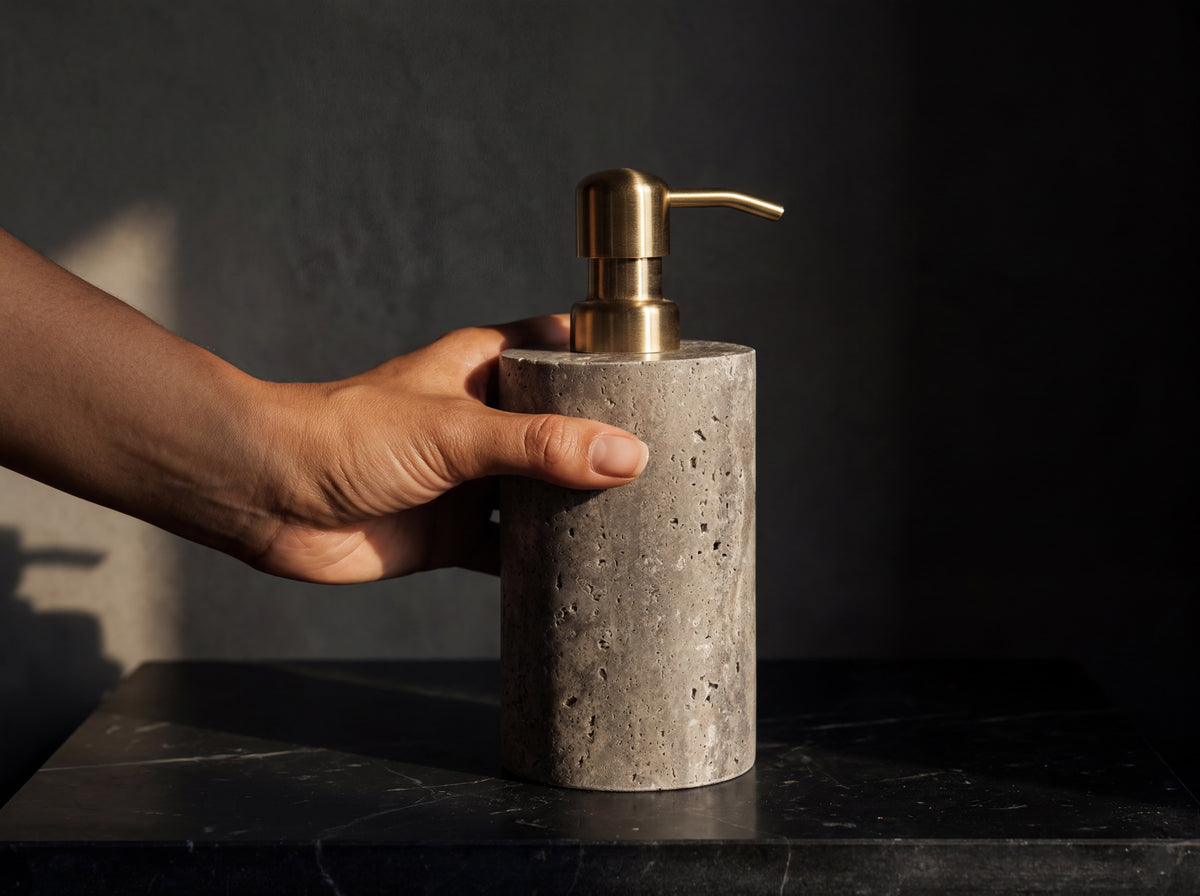 Gray marble soap dispenser held in a woman's hand to show its 17 cm size, with a dark bathroom softly blurred behind.