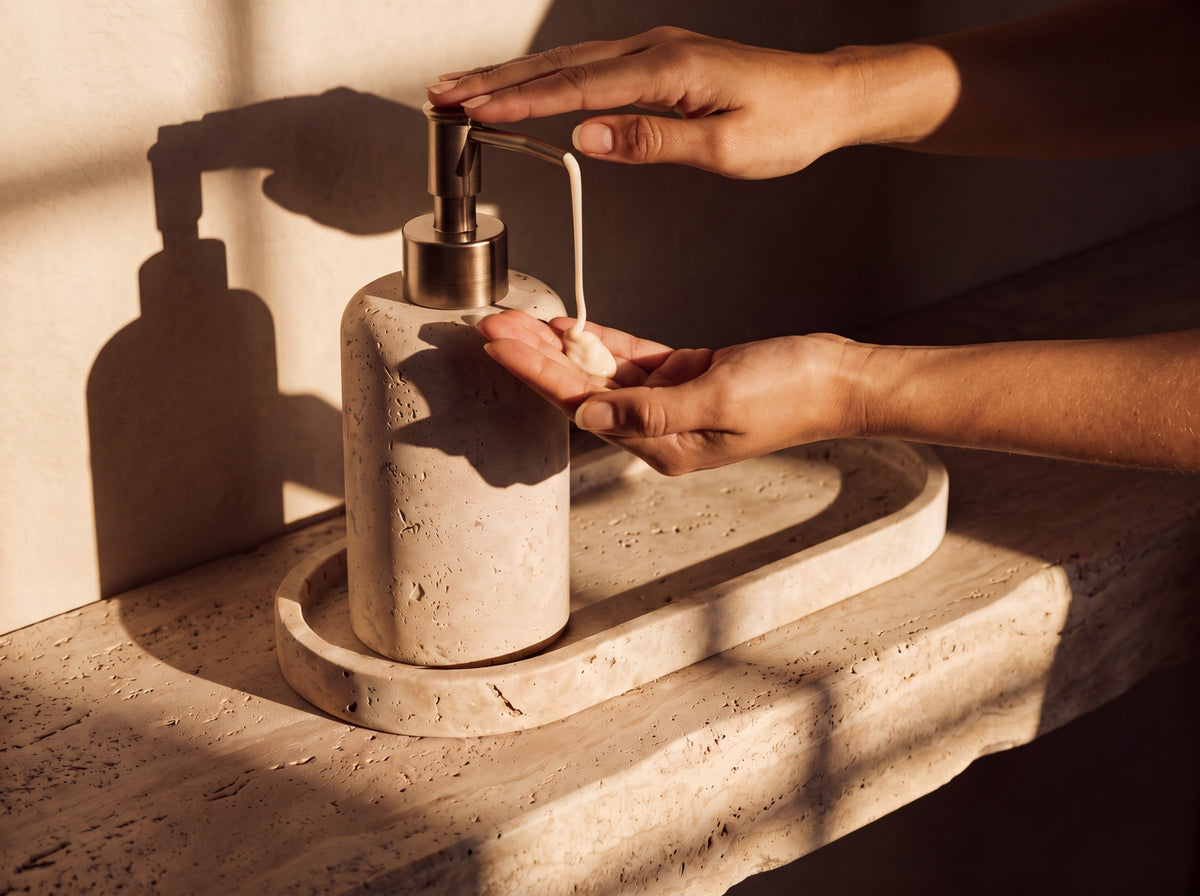 A woman's hand pressing the antique brass pump, dispensing soap into her palm over a stone basin