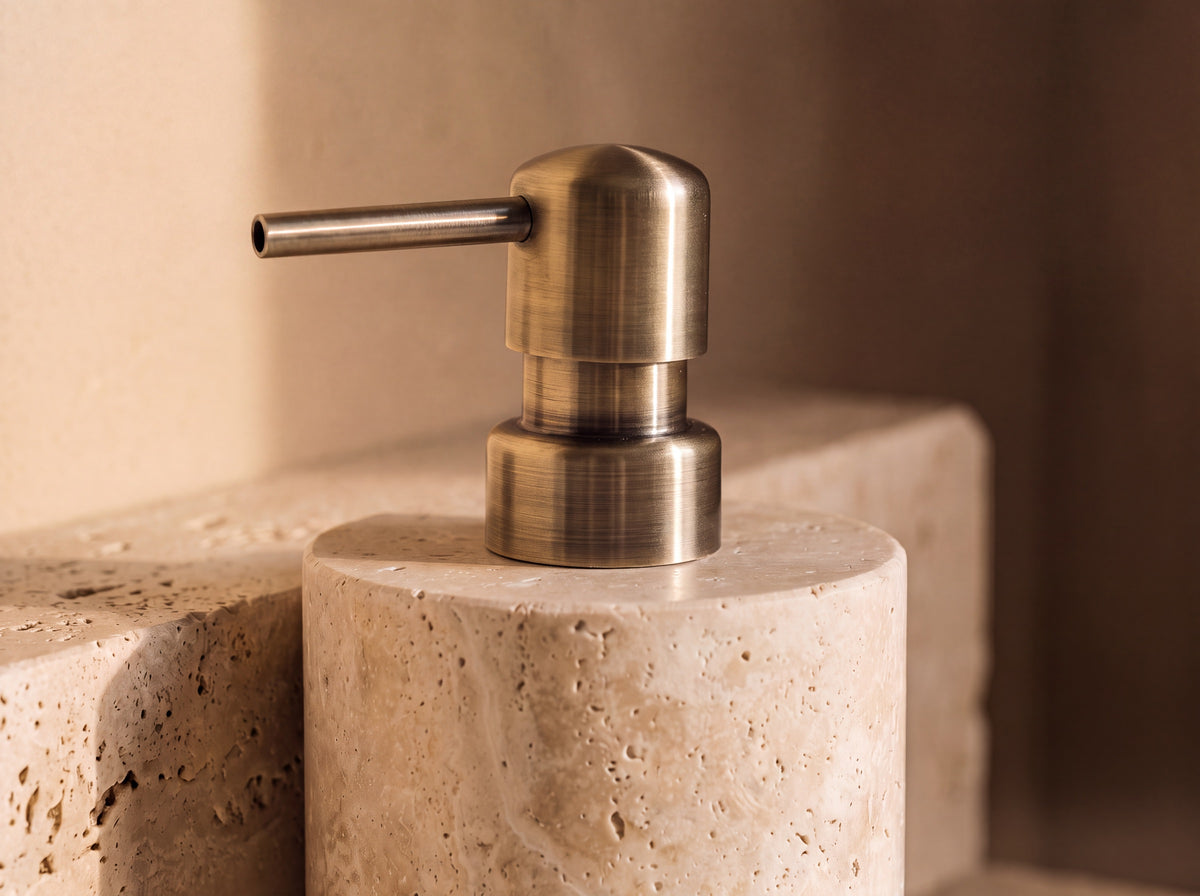 Close-up of the brushed antique brass pump and the open pores and soft banding of the cream travertine beneath it.