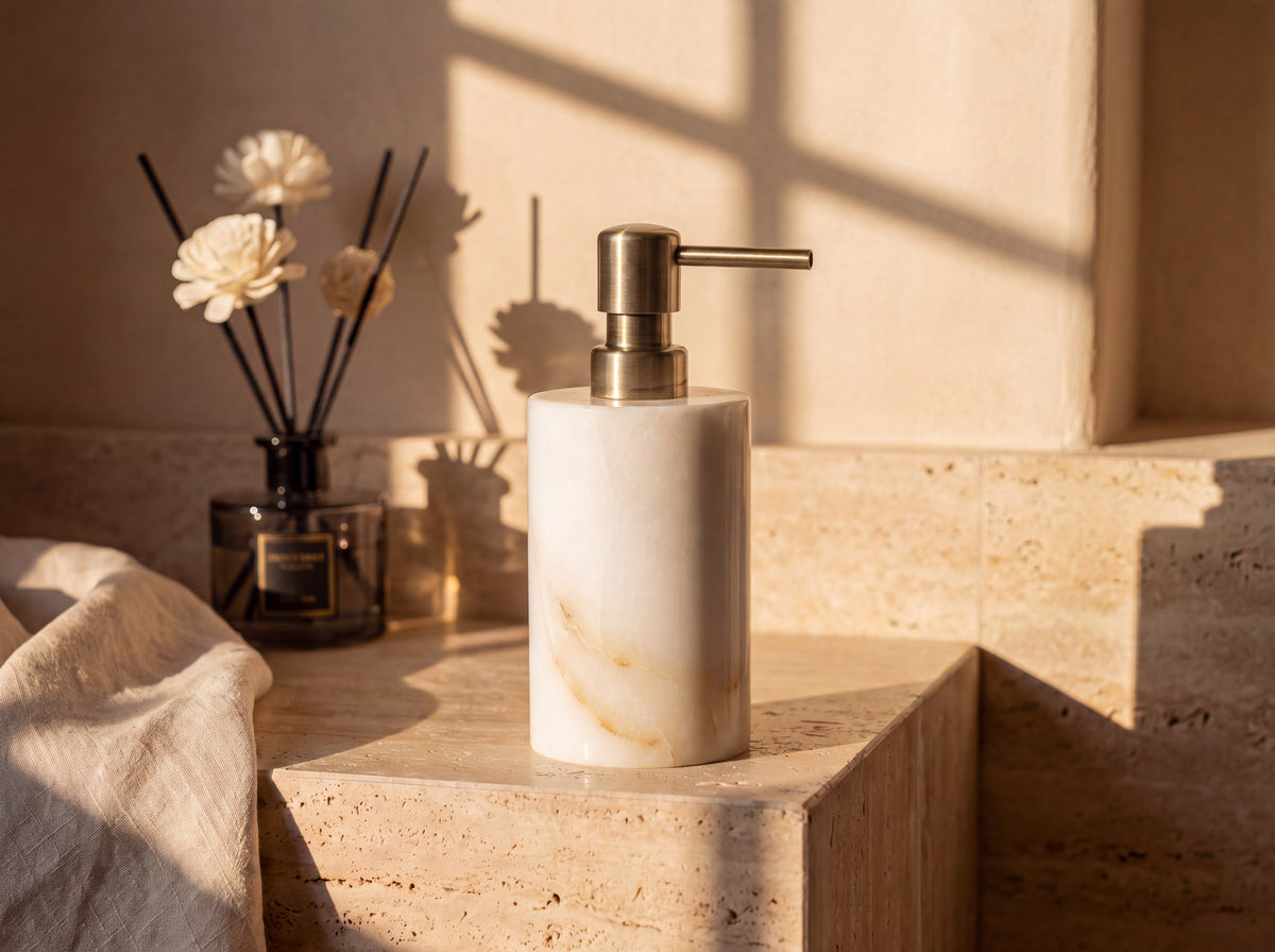 Natural white jade soap dispenser with brushed-gold pump on a sunlit travertine ledge, styled with a reed diffuser and linen.