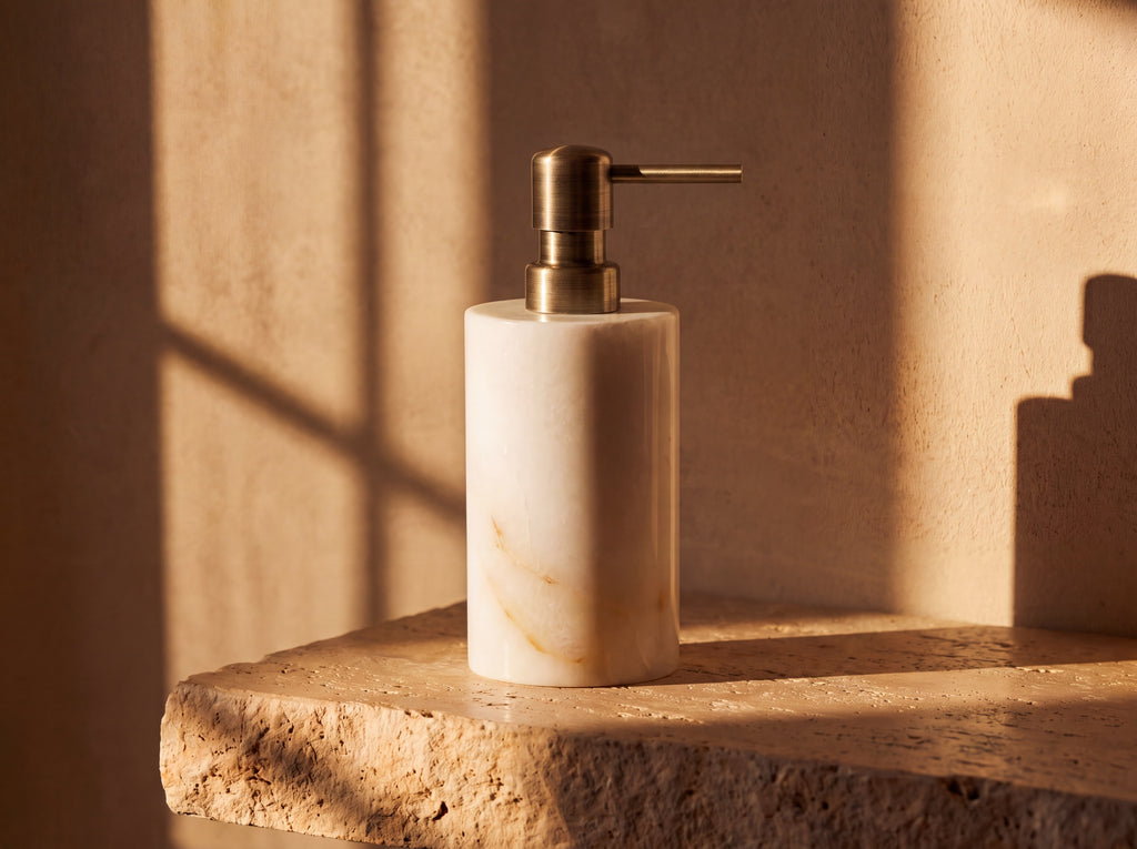 Three-quarter view of a white jade soap pump bottle with gold pump on warm stone.