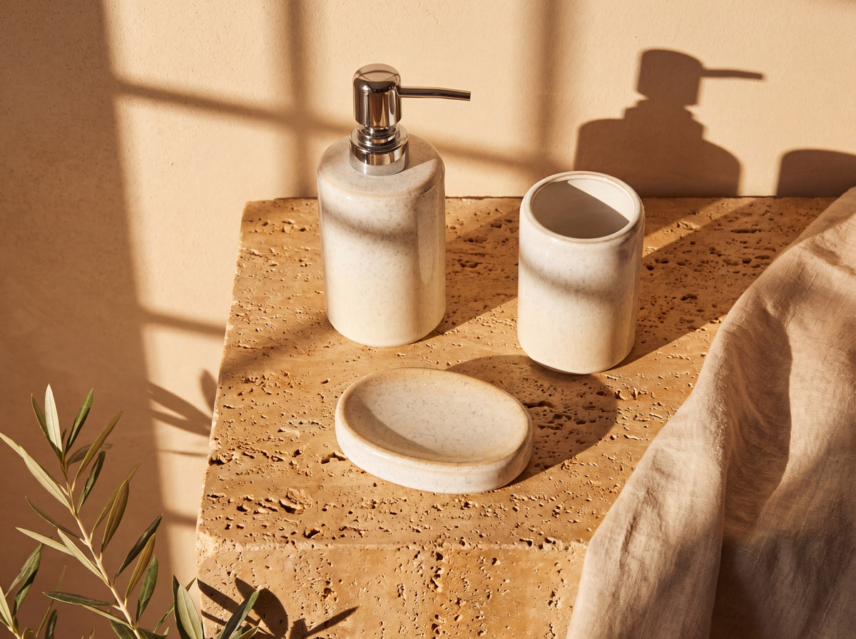 Overhead flat lay of the three-piece ceramic bath set on travertine with linen and an olive stem.