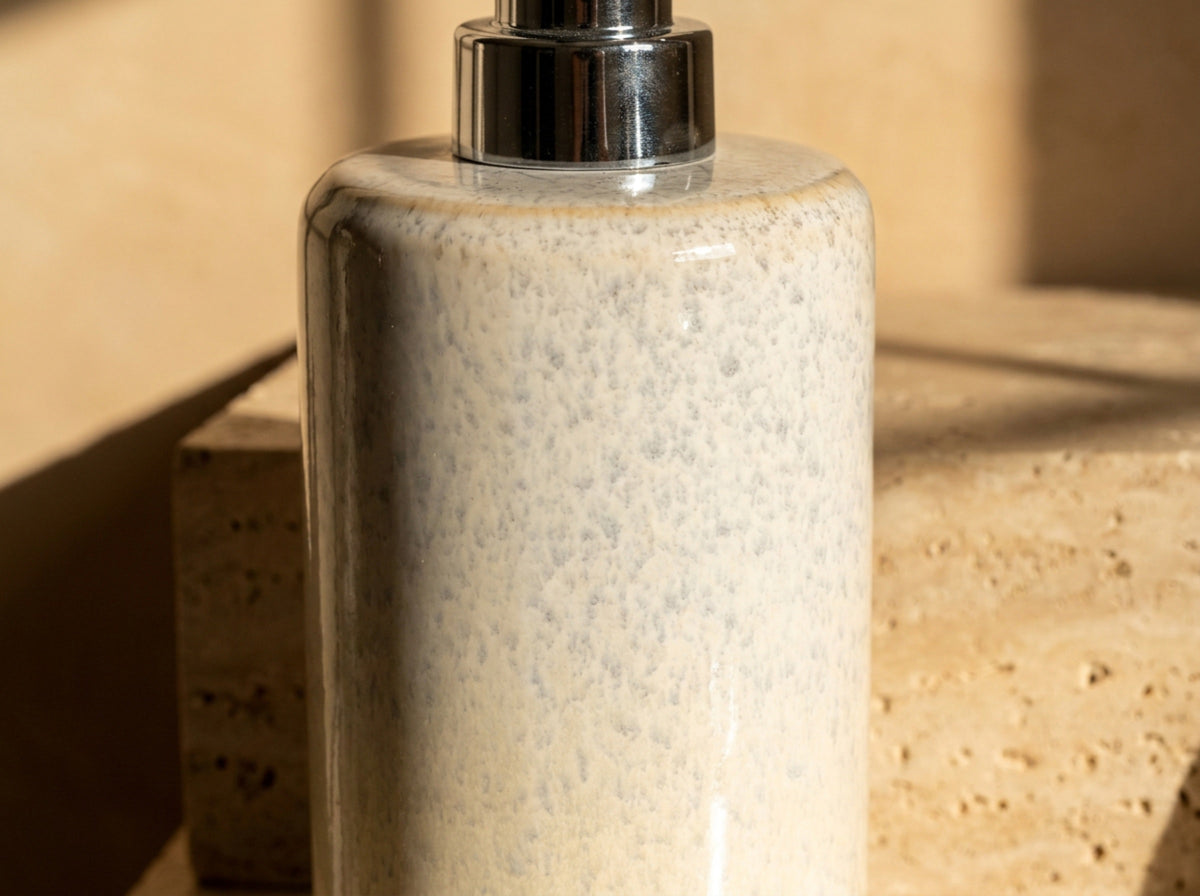 Macro close up of the reactive speckled glaze, fine pale grey flecks drifting across a creamy ivory glossy surface.