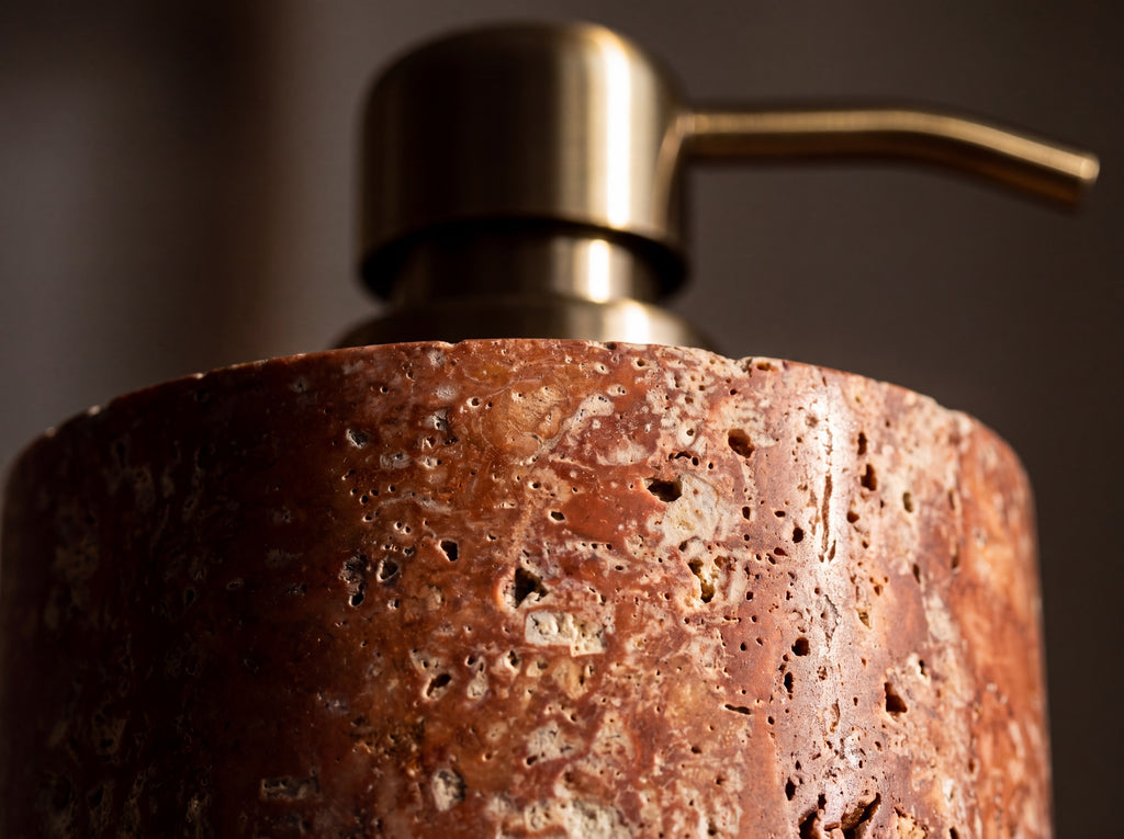 Macro close-up of red travertine stone showing natural cream pitting and porous texture on the dispenser body