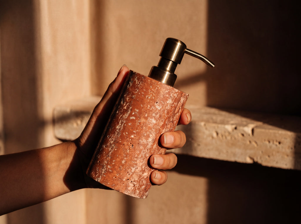 Red travertine soap dispenser held in a woman's hand showing its comfortable one-hand size