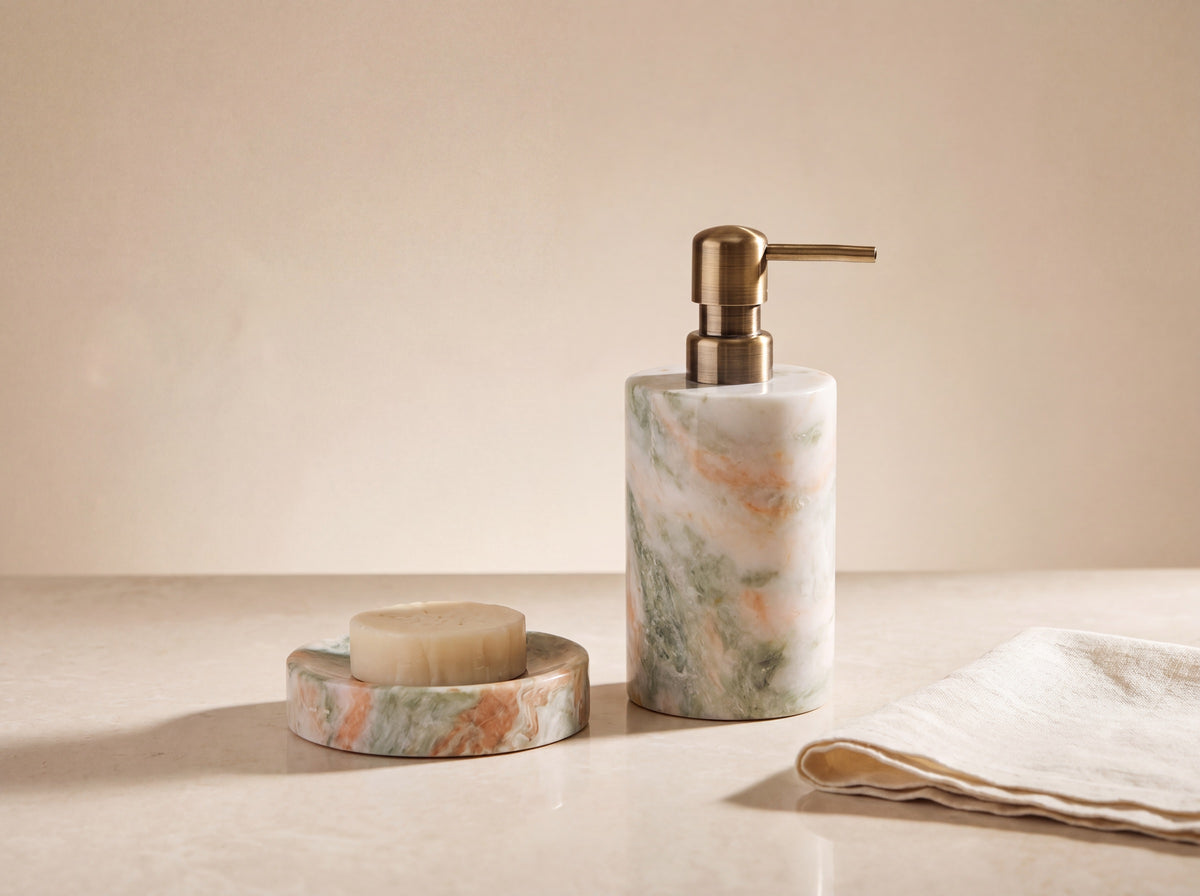 Green and peach marble soap dispenser with antique brass pump beside its matching round marble soap dish holding a cream soap bar