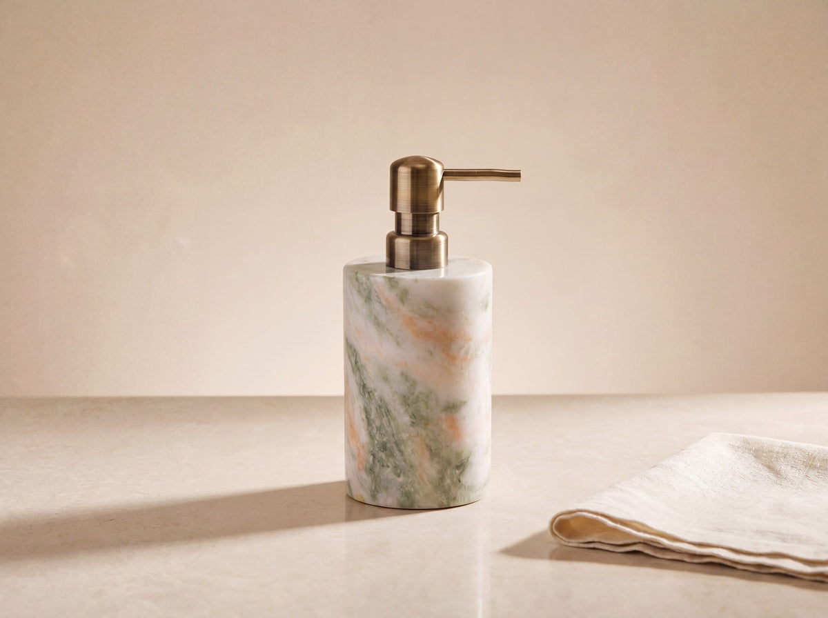 Marble soap dispenser seen from a three-quarter angle showing the curve of the stone and the brass spout