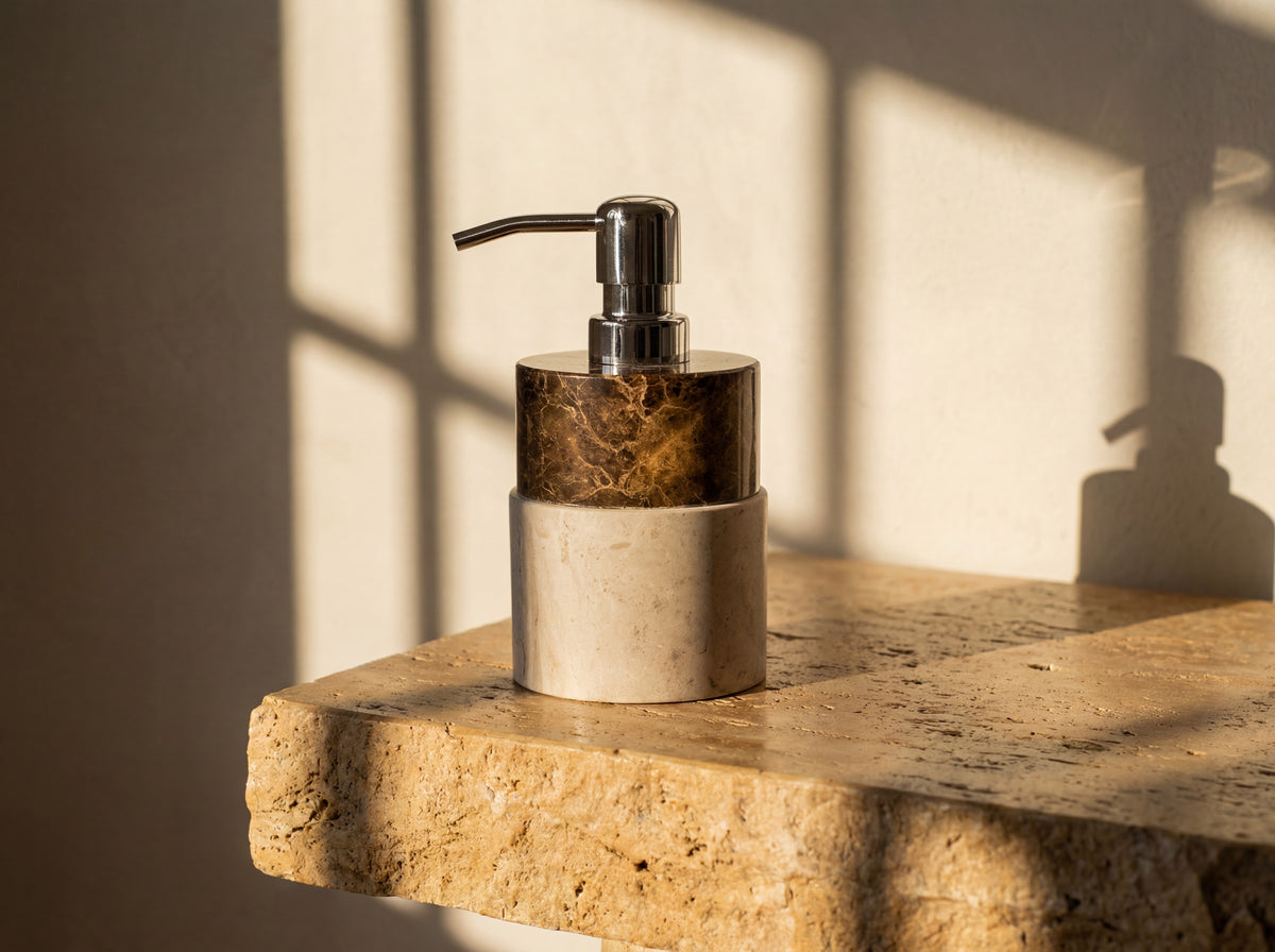 Three-quarter view of a two-tone marble soap dispenser with a polished chrome pump on warm stone.